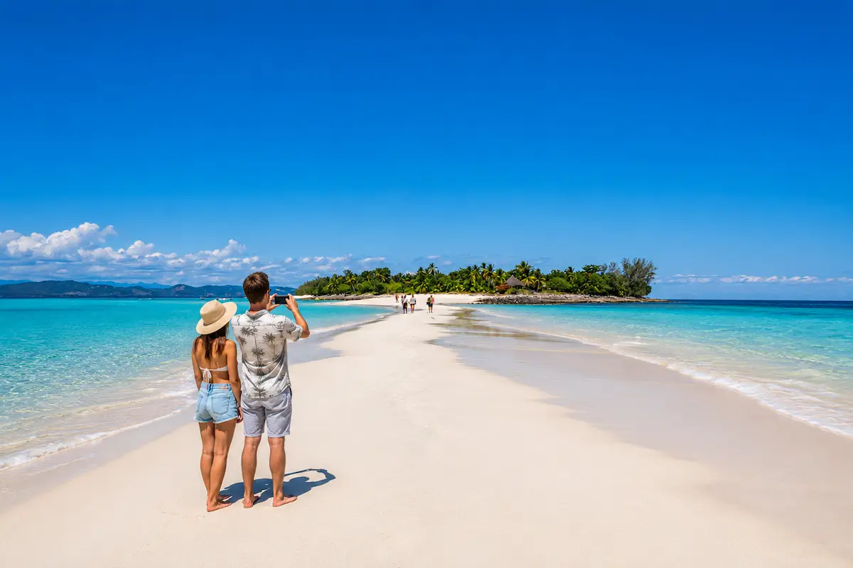 Couple taking photos on Nosy Iranja sandbank tropical beach in Madagascar